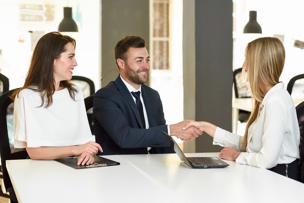 Smiling young couple shaking hands with an insurance agent or investment adviser. Three people meeting in an office reaching an agreement